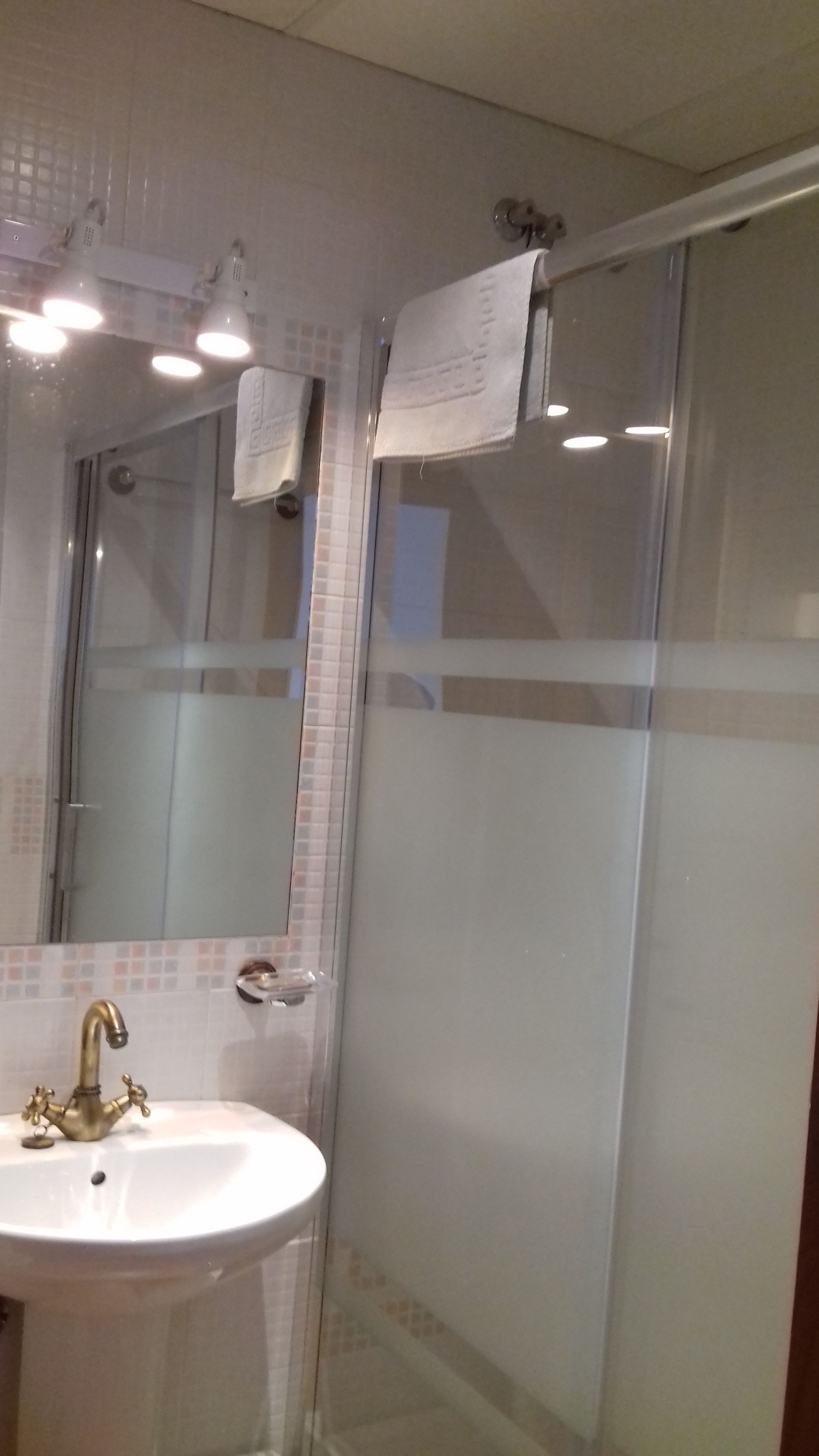 Een badkamer met een wit wastafel, een spiegel en een douchecabine van glas.