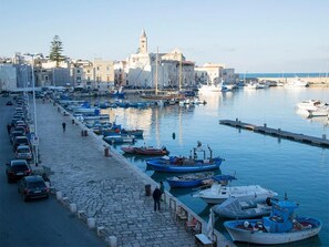 A marina with boats docked along a cobblestone waterfront, a clear sky, and buildings in the background. - Suite Home Trani (Trani)