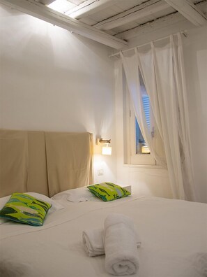 A hotel room with a bed, a window with curtains, a wall-mounted light, and a towel on the bed. - Suite Home Trani (Trani)
