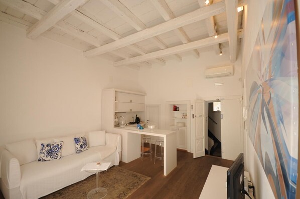 Un interior blanco con un sofá, una pequeña zona de cocina y una escalera que lleva a otro nivel.