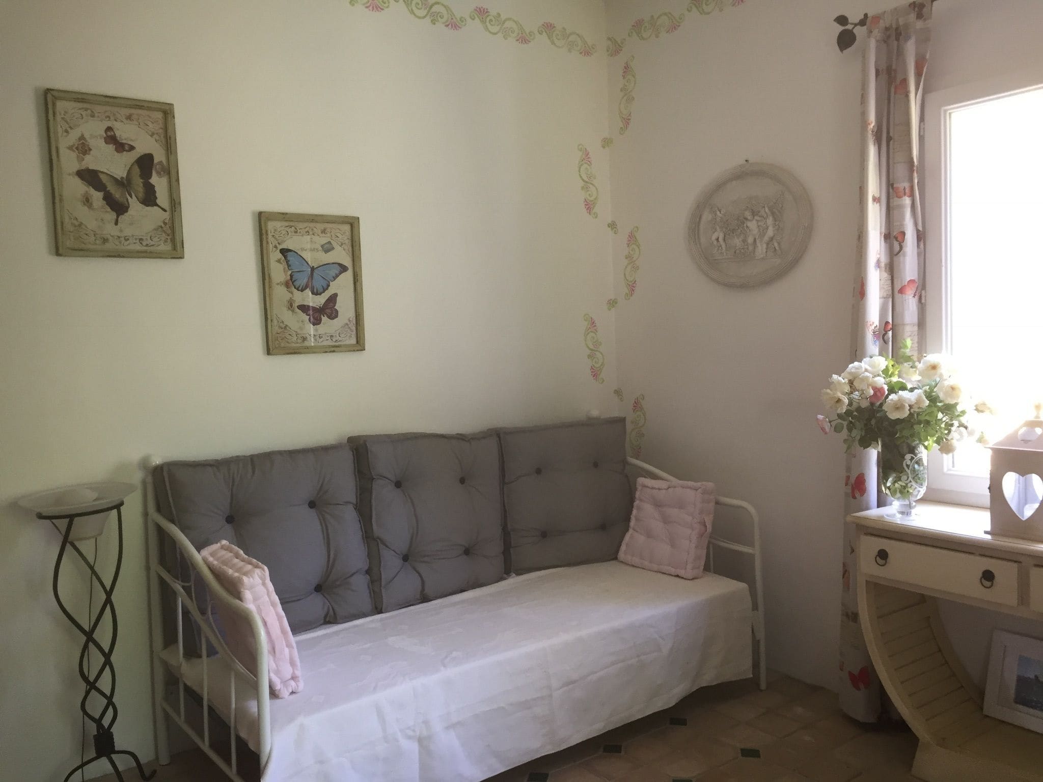 Una habitación acogedora con un sofá gris, una mesita de noche con un jarrón de flores y un plato decorativo en la pared.