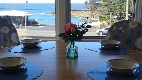 A dining table with four bowls and a vase with a single rose, positioned near a window overlooking a coastal view.