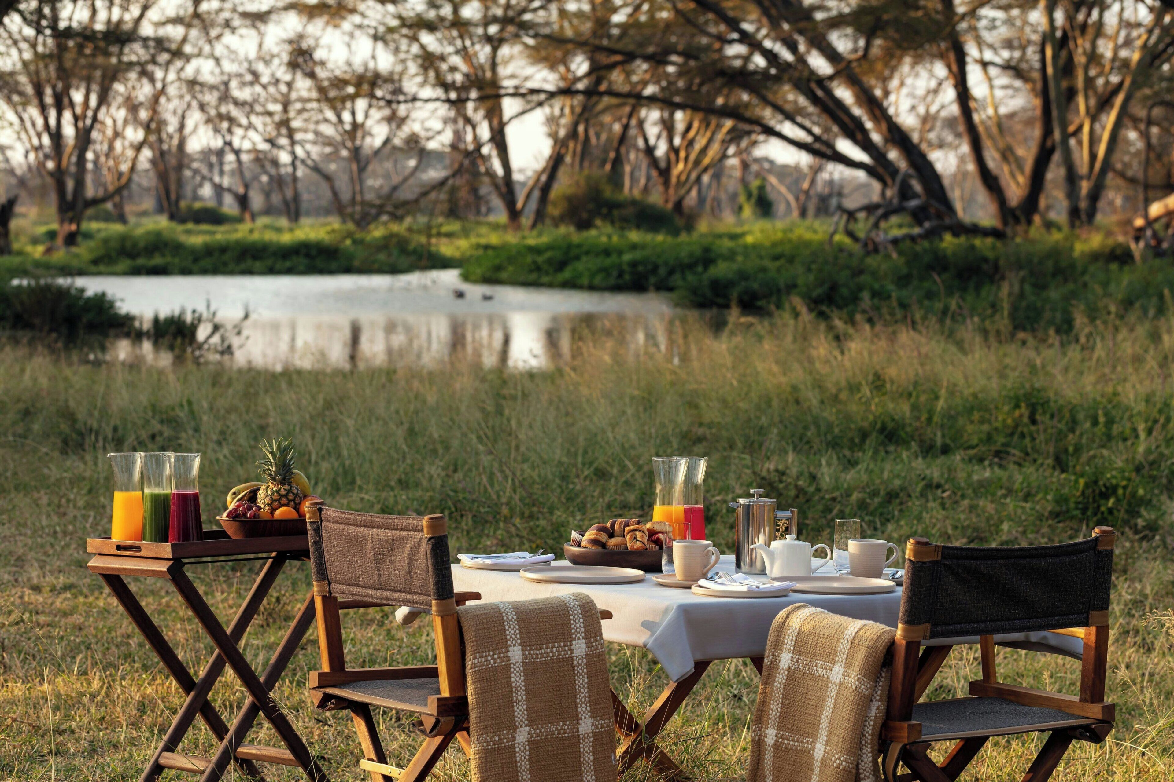 An outdoor dining setup with a table, chairs, and a variety of food and drink items.