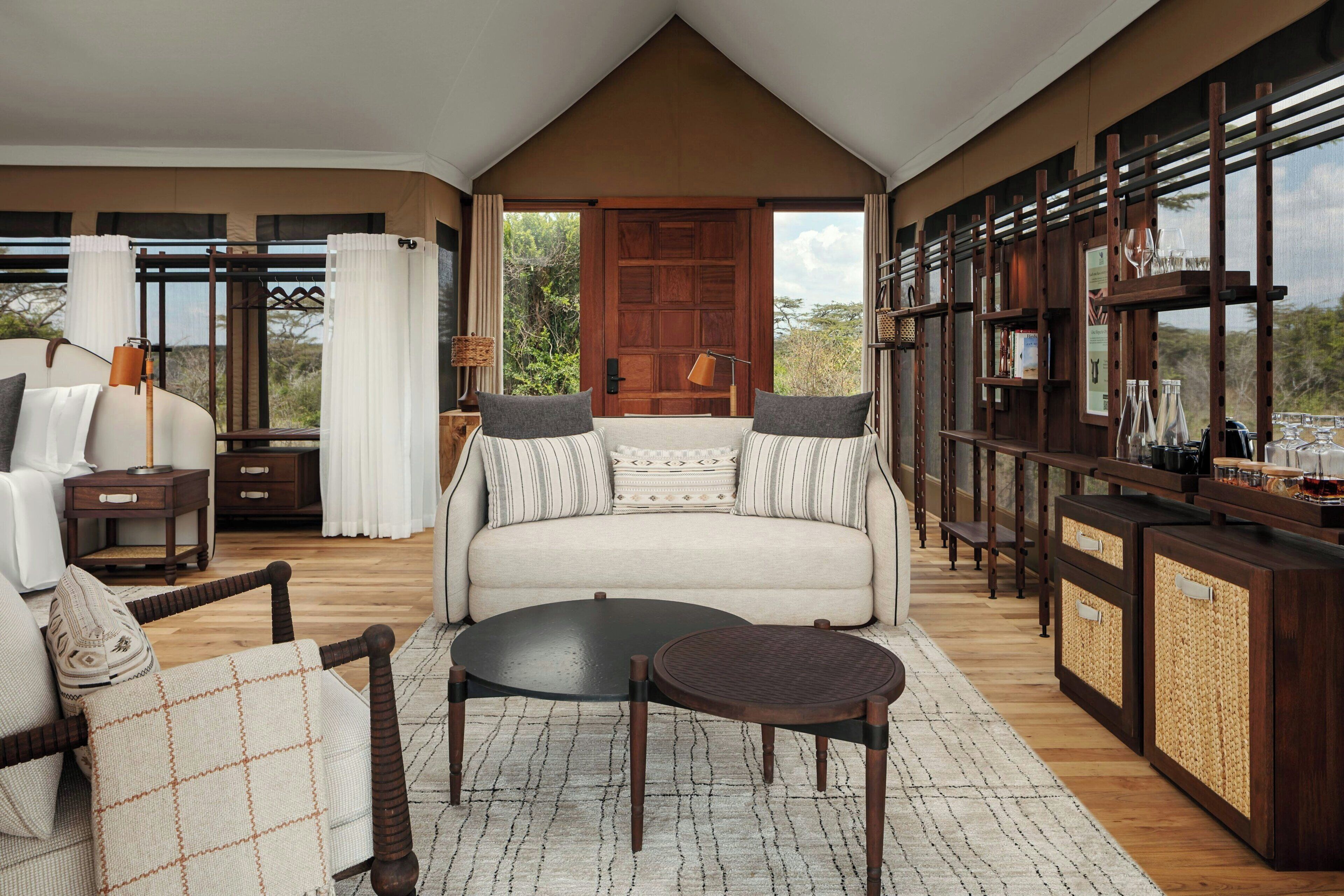 A spacious living area with a sofa, coffee table, and side tables, featuring a large wooden door and a view of the outdoors.