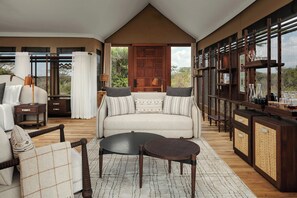 A spacious living area with a sofa, coffee table, and side tables, featuring a large wooden door and a view of the outdoors. - JW Marriott Mount Kenya Rhino Reserve Safari Camp (Laikipia County)