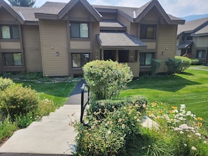 A residential building with a symmetrical facade, a covered front porch, and a well-maintained lawn with a variety of flowering plants. - Snowcreek Resort Vacation Rental 272 (Mammoth Lakes)