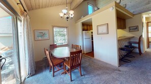 A dining area with a round table and chairs, a chandelier, and a view through a window.