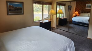 Et hotelværelse med seng, skrivebord, lampe, spejl og et vindue med persienner.