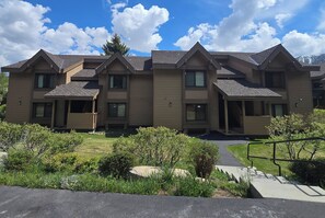 A multi-story residential building with a symmetrical design, featuring a central entrance, multiple windows, and a landscaped front yard with shrubs and a pathway. - Snowcreek Resort Vacation Rental 272 (Mammoth Lakes)