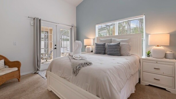 A bedroom with a bed, nightstands, a chair, and a sliding glass door leading to an outdoor area. - Indian Ridge - Pool Home Spa, Newly Renovated (Kissimmee)
