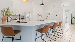 A modern kitchen with a central island, bar stools, pendant lighting, and white cabinetry. - Indian Ridge - Pool Home Spa, Newly Renovated (Kissimmee)