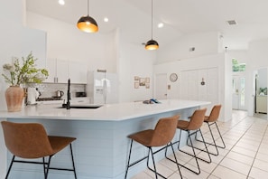 Een moderne keuken met een centraal eiland, barkrukken, hanglampen en witte kasten.