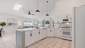 A modern kitchen with white cabinetry, a central island, a ceiling fan, pendant lights, a microwave, an oven, and a refrigerator. - Indian Ridge - Pool Home Spa, Newly Renovated (Kissimmee)