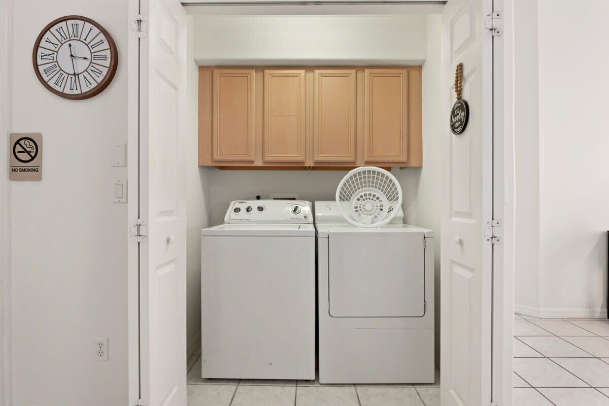 A laundry room with a washing machine, dryer, wooden cabinets, a fan, a clock, and a 'No Smoking' sign.