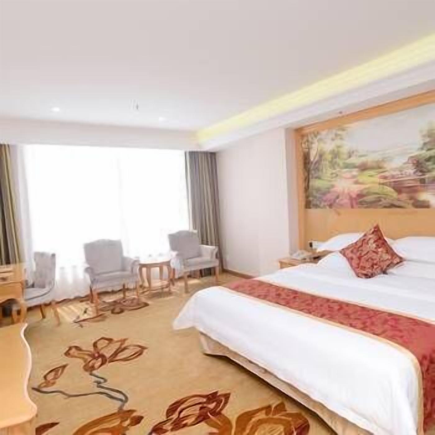 Habitación de hotel con una cama grande, un cuadro en la pared y vistas al exterior.