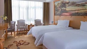 Habitación de hotel con dos camas, un cuadro en la pared, un escritorio con silla y vistas al exterior por la ventana.