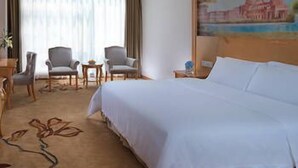 Una habitación de hotel con una cama grande, dos sillones, una mesita y un cuadro en la pared.