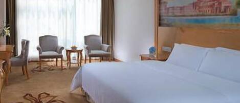 A hotel room with a large bed, two armchairs, a small table, and a painting on the wall.