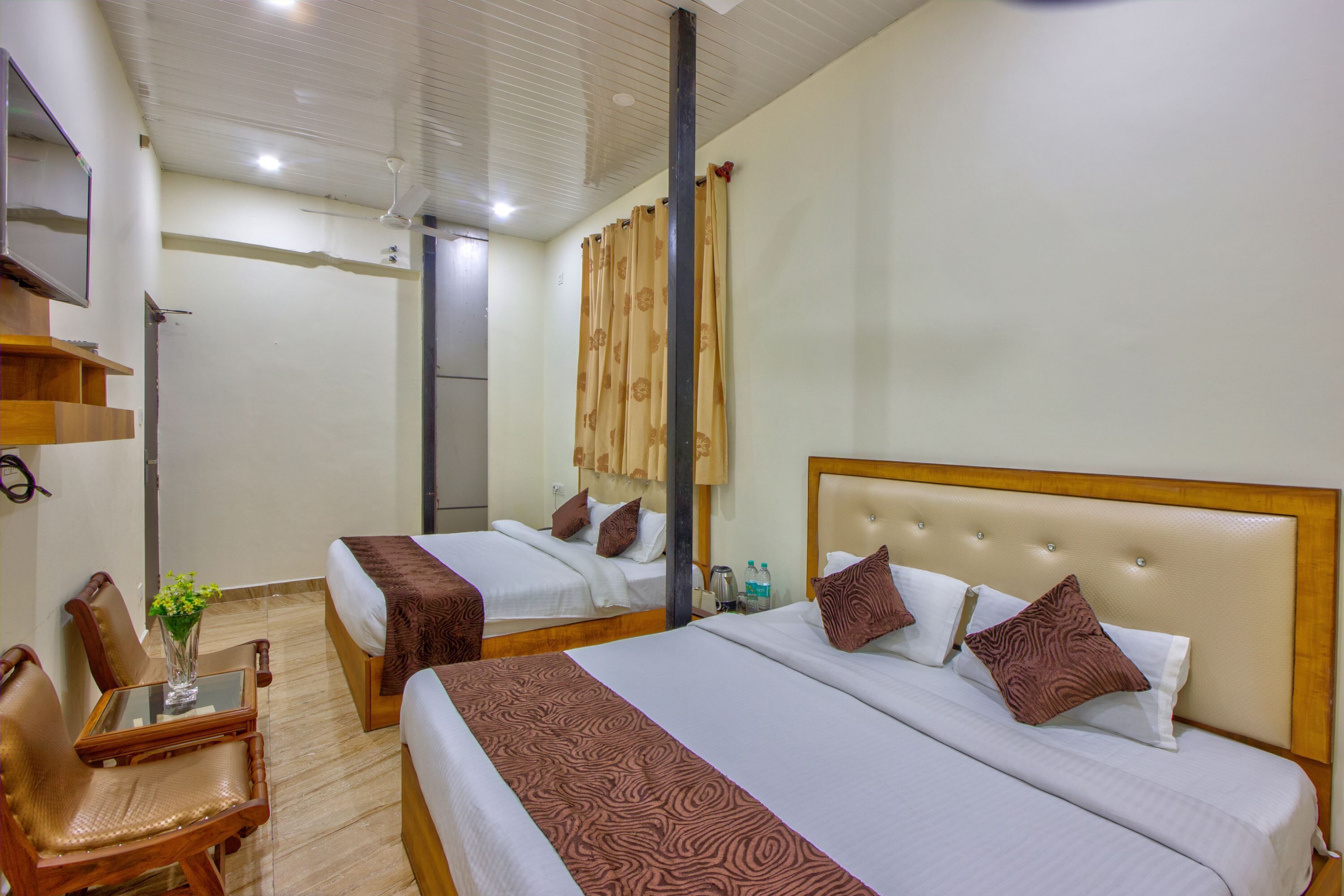 A hotel room with two beds, a wooden chair, a small table with a vase, and a mirror on the wall.