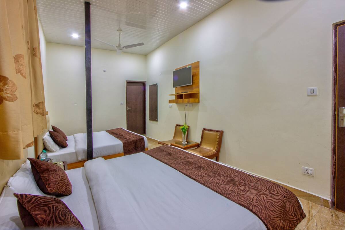 A hotel room with two beds, a TV mounted on the wall, a ceiling fan, and a door.