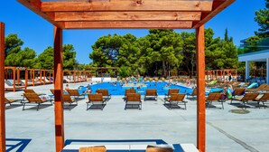 Zona de piscina amb pèrgoles de fusta, gandules i un cel blau clar.