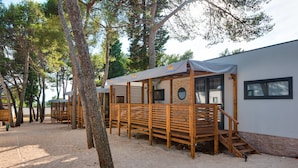 Filera de cabanes de fusta amb un porxo cobert, terra sorrenca i arbres al fons.