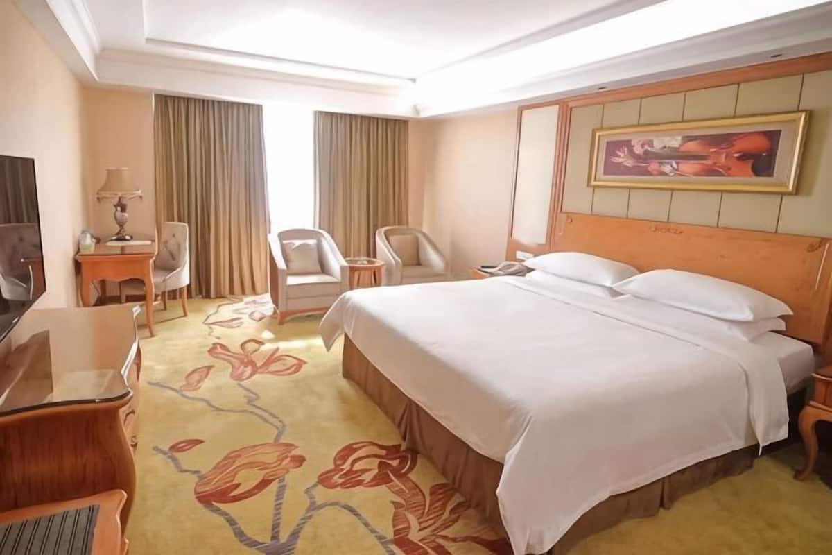 Quarto de hotel com uma cama, uma escrivaninha, uma cadeira, uma televisão e um quadro na parede.