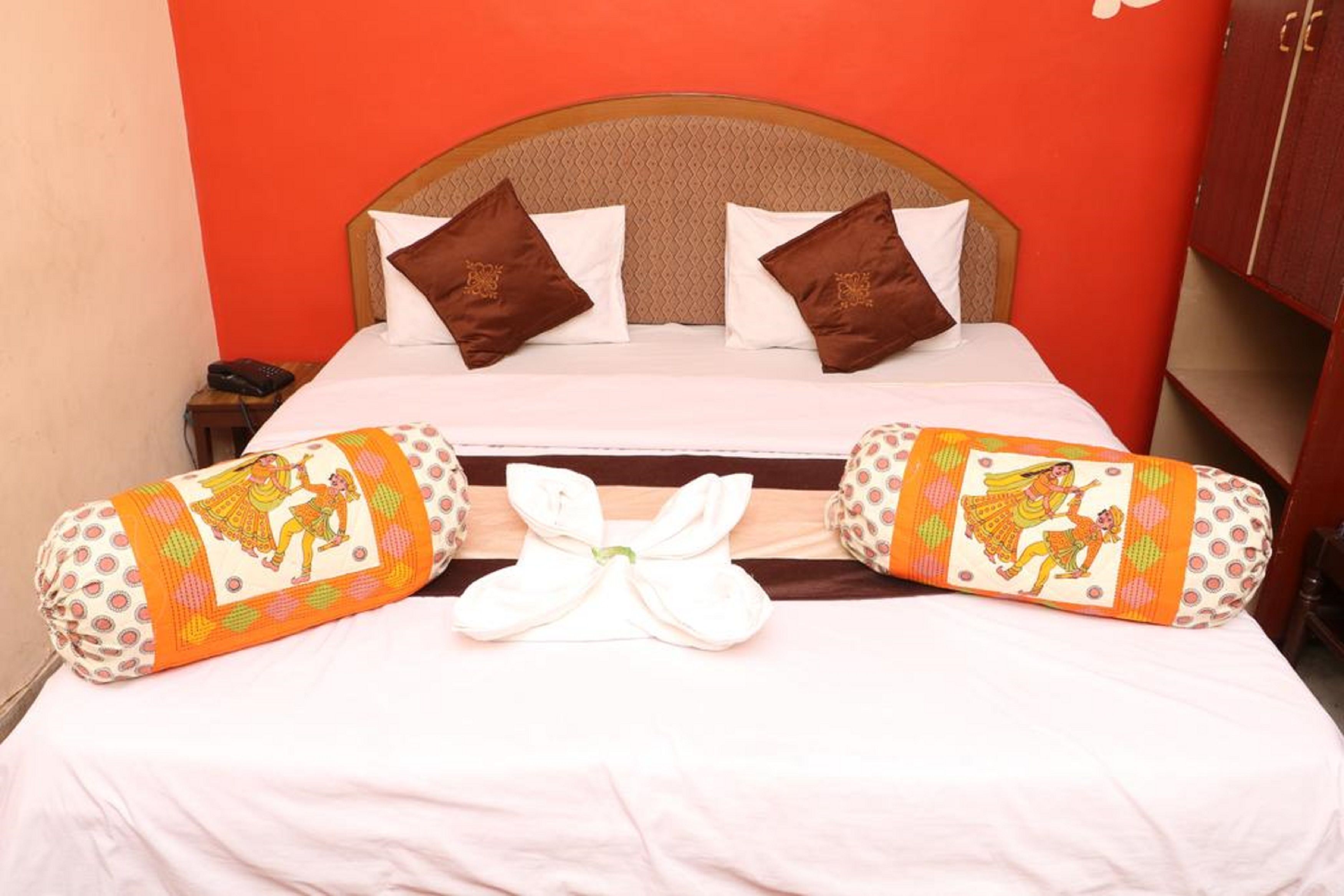 A hotel room with a bed, pillows, and a decorative bow on the bed.
