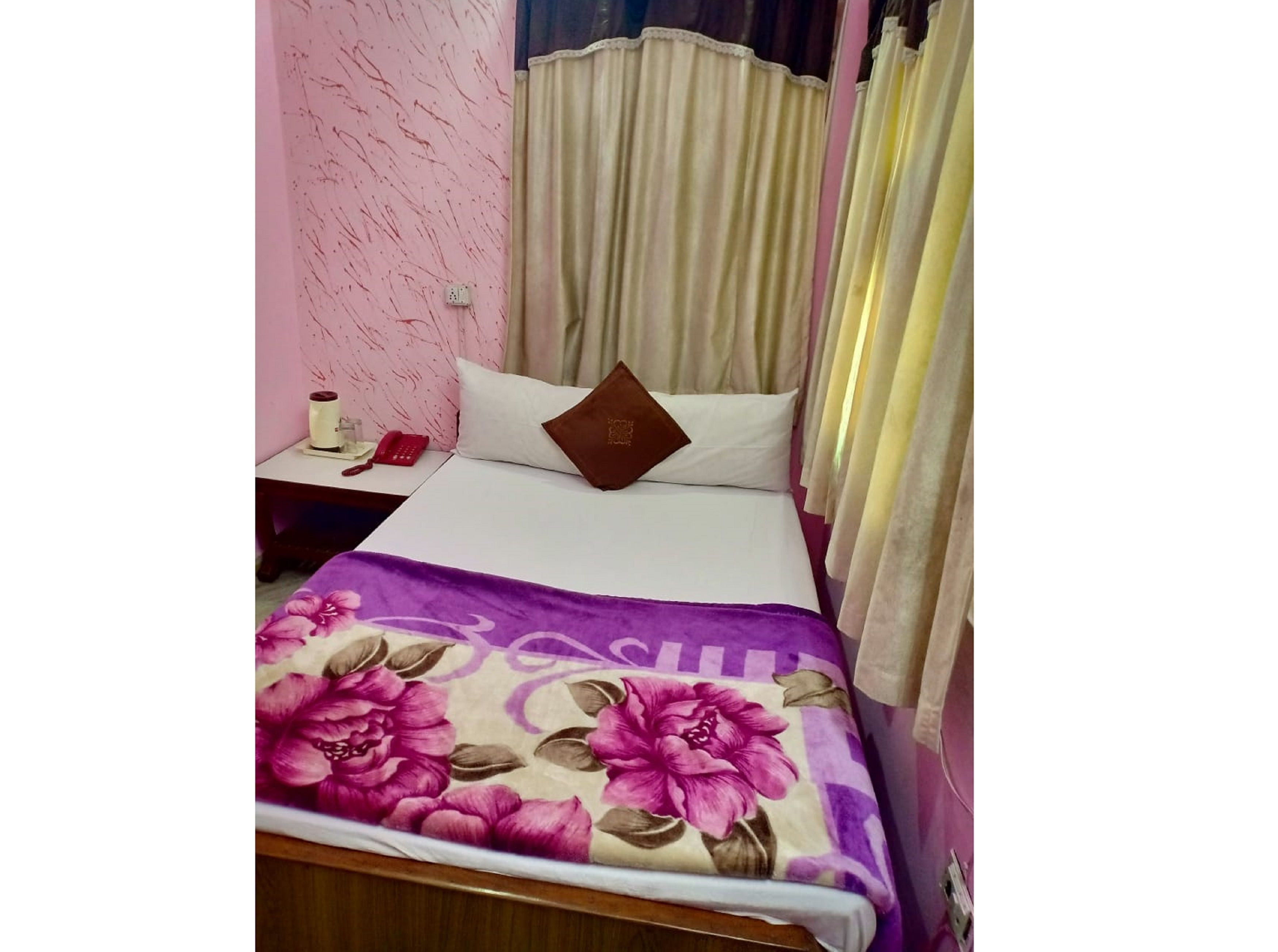 A bed with a floral bedspread, a nightstand with a telephone, and curtains.
