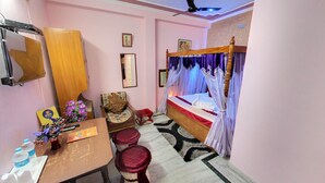 Une chambre à coucher avec un lit à baldaquin, un bureau avec une chaise, une petite table sur laquelle est posé un vase de fleurs et un miroir accroché au mur.