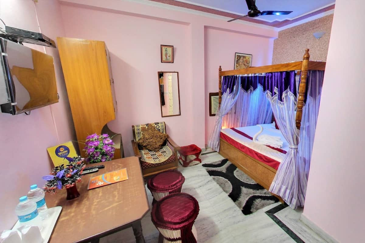 Un dormitorio con cama con dosel, un escritorio con silla, una mesita con un florero y un espejo en la pared.