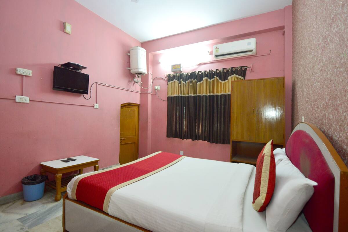 Una habitación rosa con una cama, un televisor, aire acondicionado y una cortina.