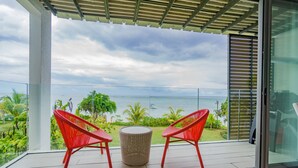 Varanda com duas cadeiras vermelhas e uma mesa redonda pequena, com vista para a água e vegetação.