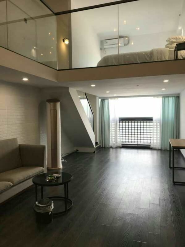 A spacious living area with a high ceiling, a sofa, a coffee table, and a staircase leading to an upper level.