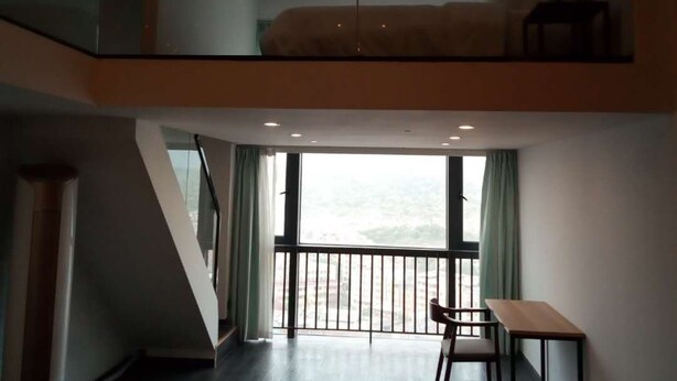 A modern loft-style room with a glass ceiling, a bed, a desk, and a view of the city. - Xitishu Hotel Apartment (Guangzhou)