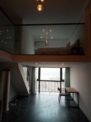 A modern loft-style room with a glass ceiling, a bed, a desk, and a view of the city.