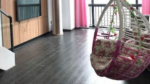 A modern living room with a wooden panel wall, a large window with pink curtains, a hanging chair, and a television. - Xitishu Hotel Apartment (Guangzhou)