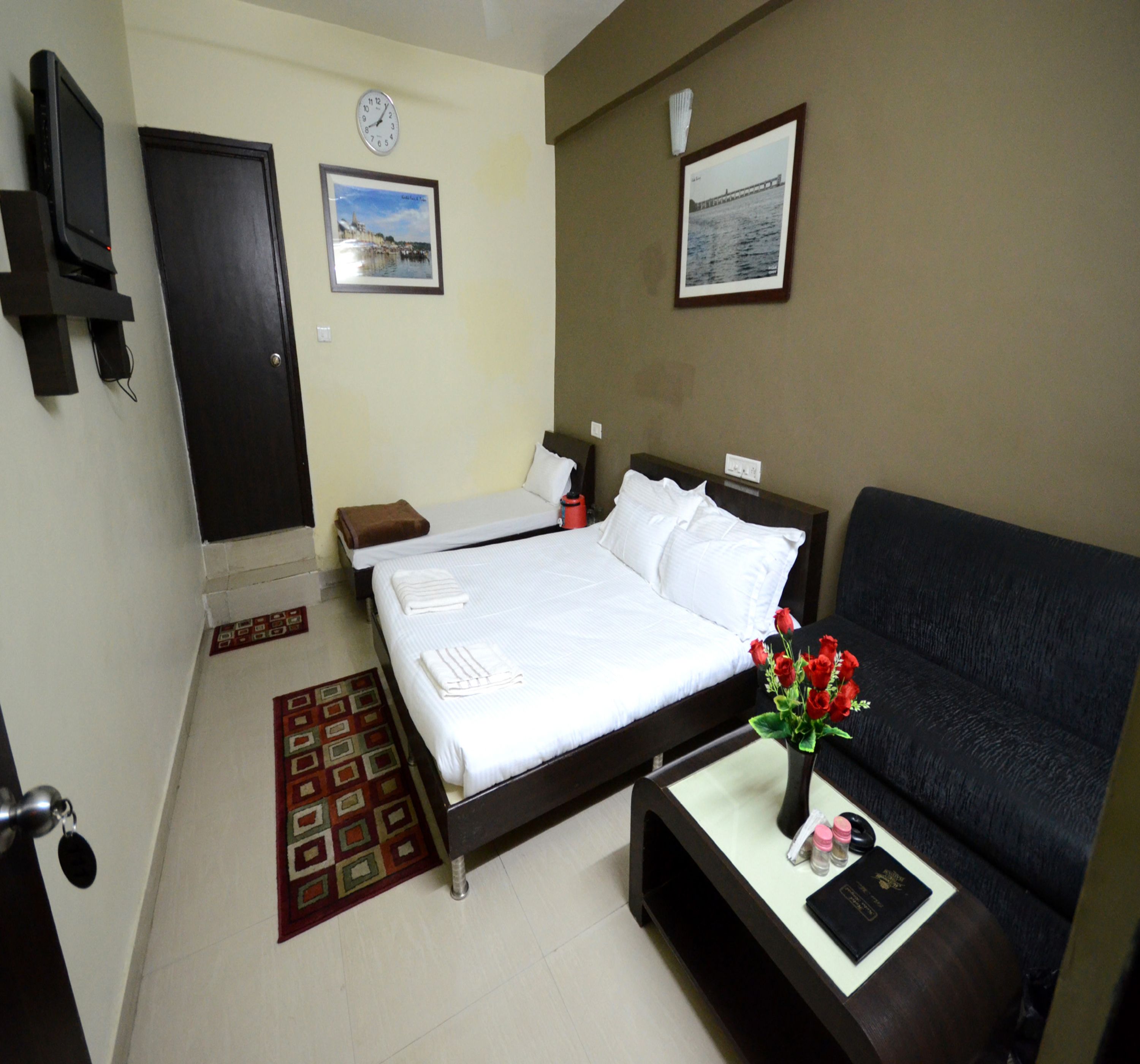 A hotel room with a bed, a sofa, a small table with a vase of flowers, and two framed pictures on the wall.
