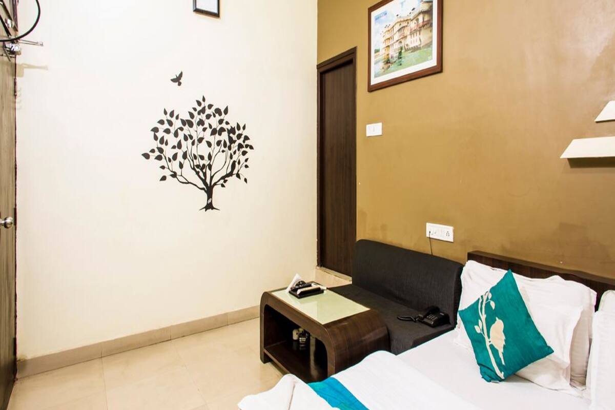 A hotel room with a bed, a desk, a chair, a clock, and a wall decoration of a tree with a bird.