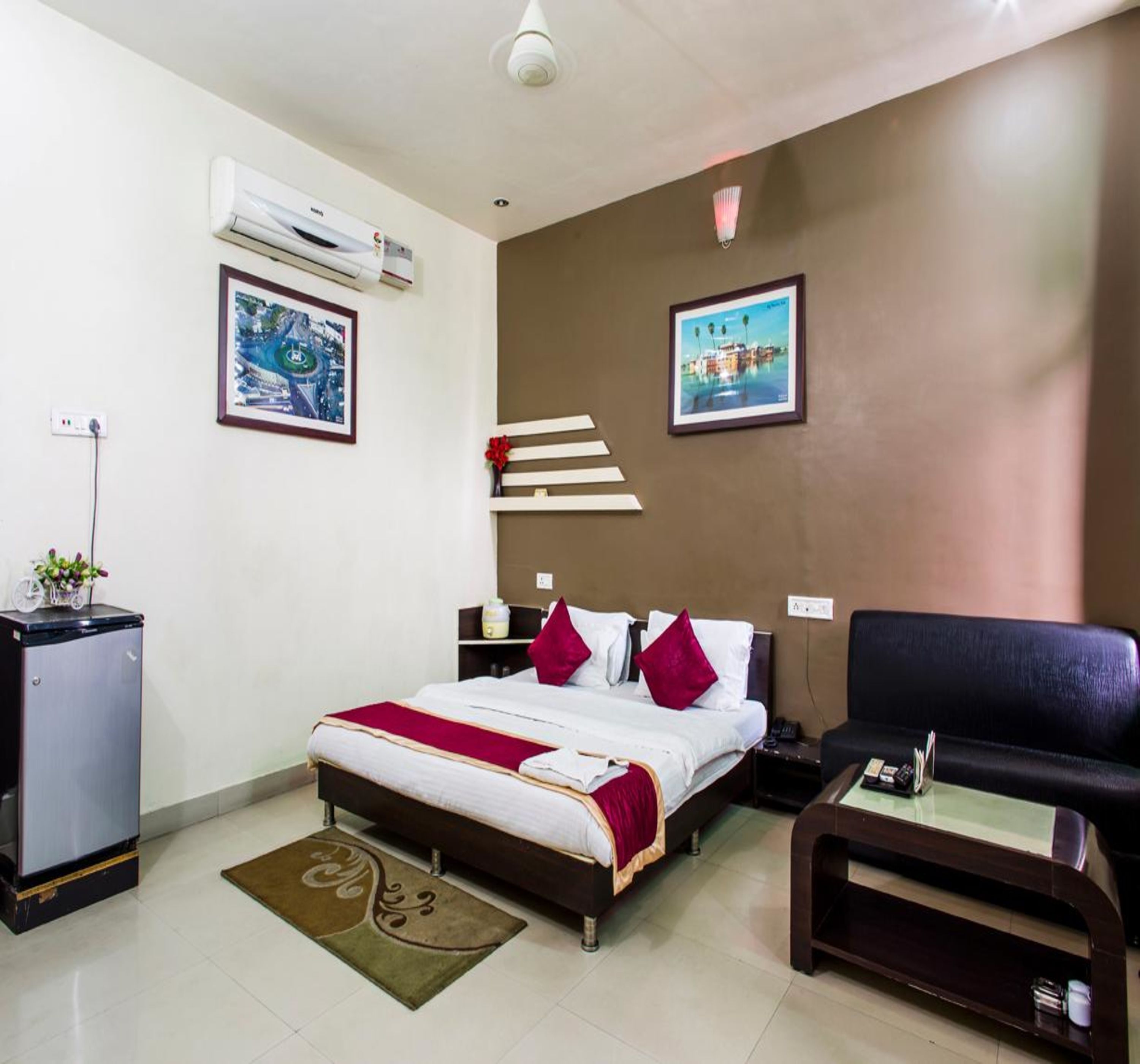 A hotel room with a bed, a desk, a chair, a small refrigerator, and two wall-mounted air conditioners.