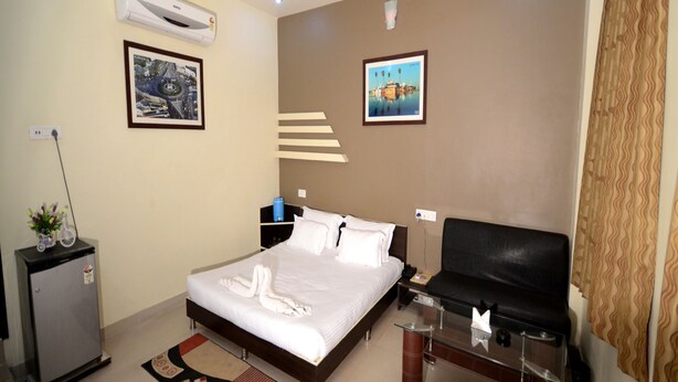 Hotelkamer met een bed, bureau, stoel, televisie, plafondventilator, airconditioning en een kleine koelkast.