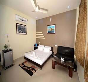 Hotelkamer met een bed, bureau, stoel, televisie, plafondventilator, airconditioning en een kleine koelkast.