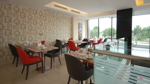 A modern restaurant with a patterned wallpaper, red and black chairs, and a glass railing overlooking a street. - Imamoglu Pasa Hotel - Boutique Class (Kocasinan)