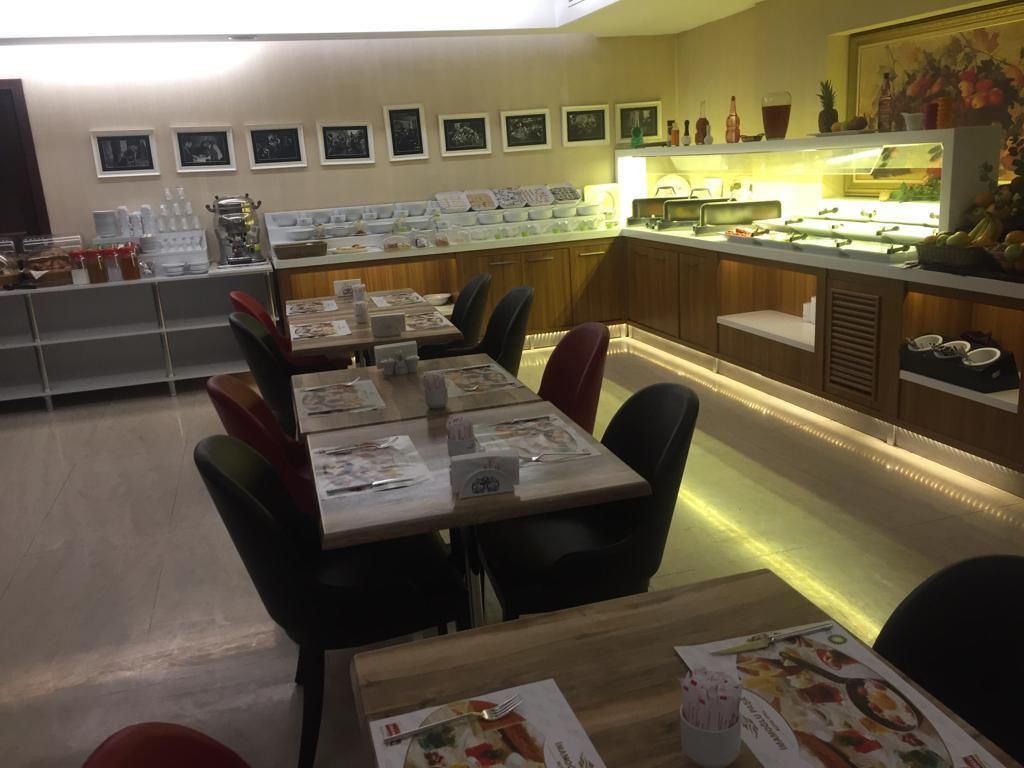 Um restaurante com várias mesas e cadeiras, um balcão com alimentos à mostra e quadros nas paredes.