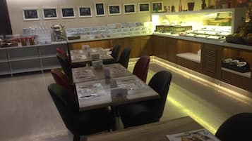 Um restaurante com várias mesas e cadeiras, um balcão com alimentos à mostra e quadros nas paredes.