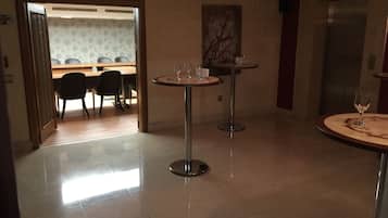 A hotel lobby with two round tables, a dining area in the background, and an elevator.
