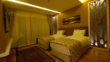 Habitación de hotel con dos camas, un escritorio, una silla, un ventanal con cortinas, un panel decorativo en la pared y una alfombra.