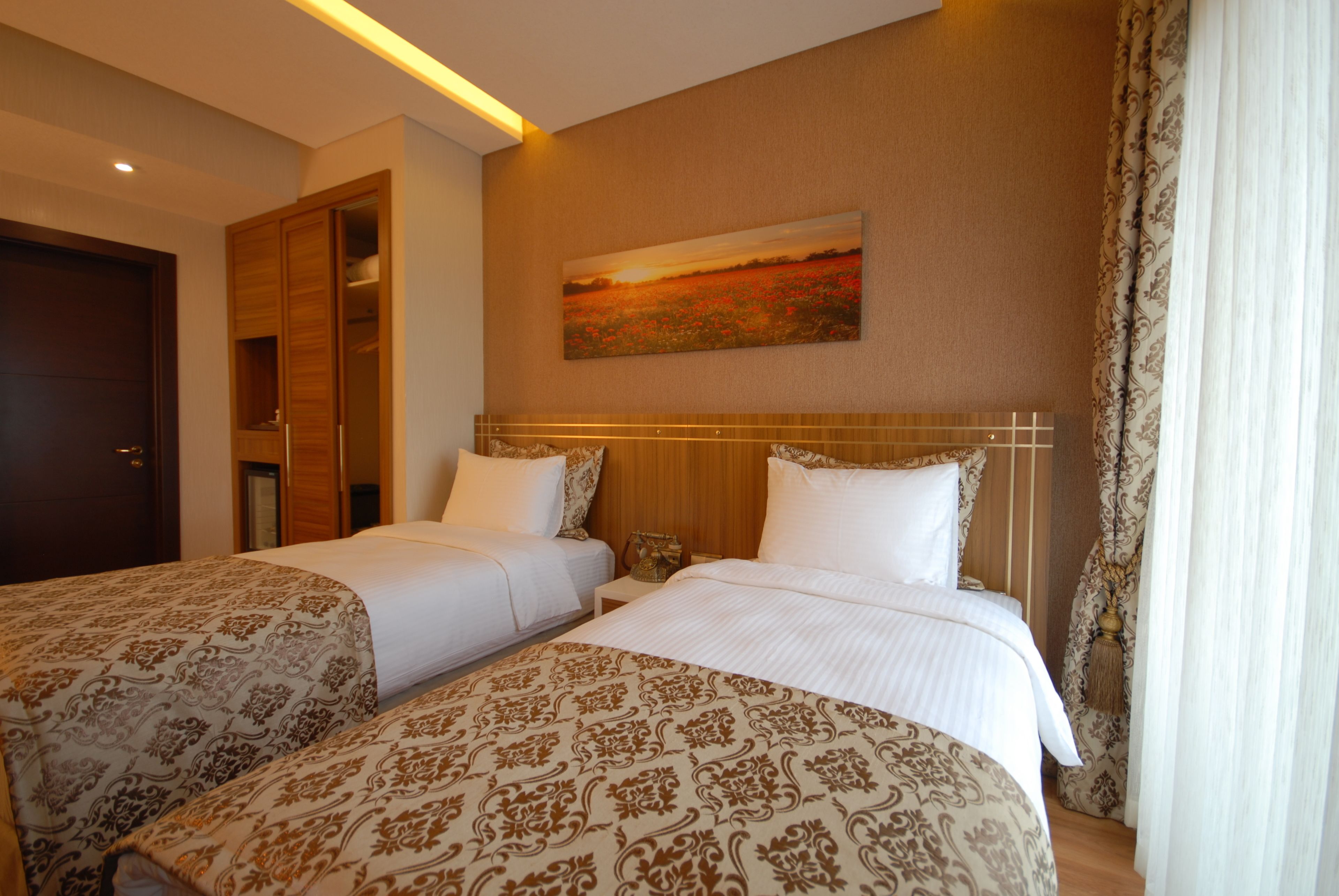 A hotel room with two beds, a wooden wardrobe, a painting on the wall, and a curtain on the window.