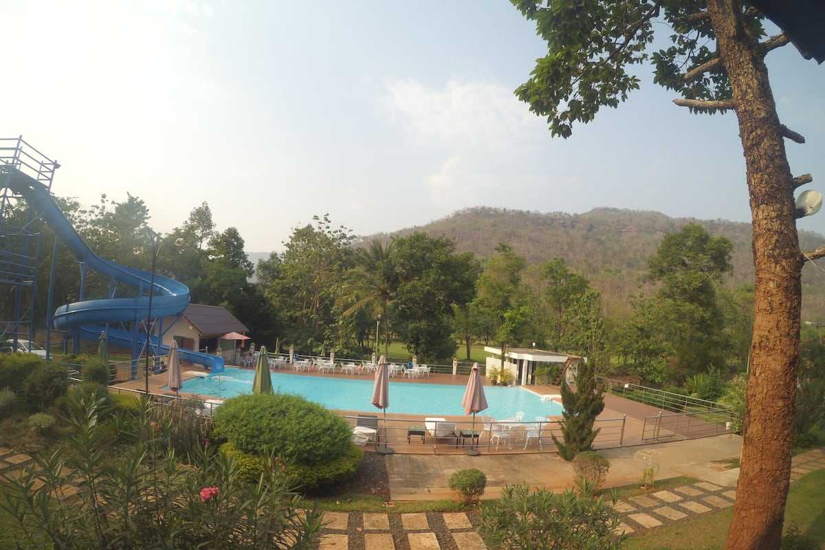 Uma área de piscina com um toboágua, rodeada por vegetação exuberante e vista para colinas.