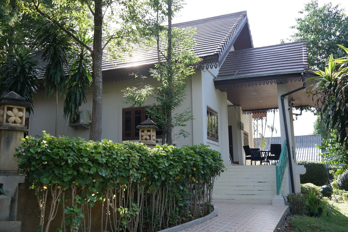 Uma casa de dois andares com telhado de telhas, varanda coberta e escada que leva à entrada.